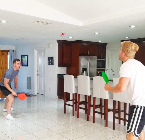 Friends playing jazzminton paddle ball indoors by the kitchen
